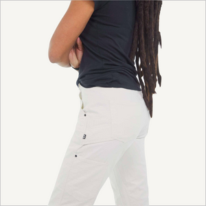 Side view of model wearing Women's Dovetail Anna Taskpant in white. Model is wearing a black tee and is visible from her shoulder to knee. 