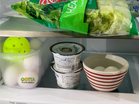 eggs and a gotta pickleball in a bin alongside yogurt and bag of salad inside refrigerator on shelves