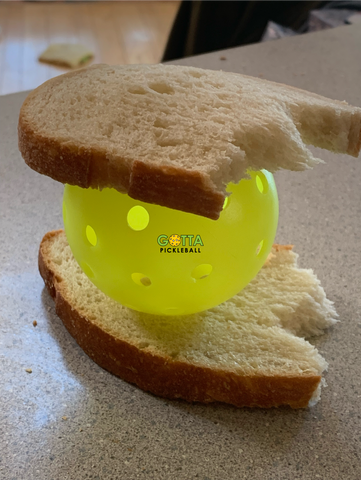 A pickleball in-between two slices of brown bread on kitchen counter gotta pickleball