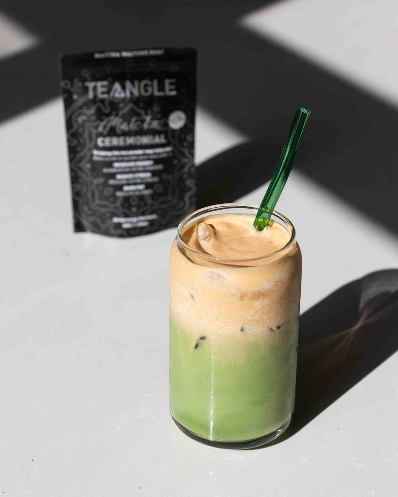 A tall glass filled with iced green matcha latte, crowned with a generous dollop of creamy pumpkin cold foam, sitting on a counter