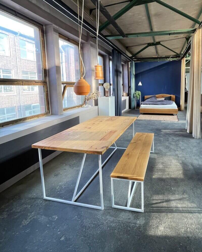 Table en bois massif et en arrière-plan notre lit en bois massif au design industriel avec glissières en acier
