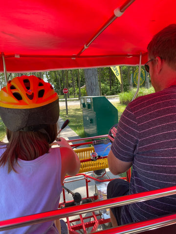 young girl and man driving a 4 person bike at Presque Isle State Park with red awning over them 