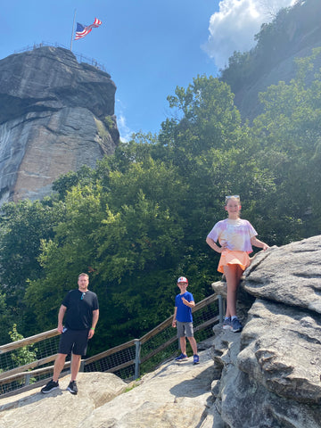 man and two young children standing on rocks with mountains and trees in background at Chimney Rock North Carolina 