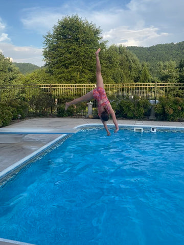 young girl cartwheeling off diving board of blue inground pool with Blue Ridge Mountains in background