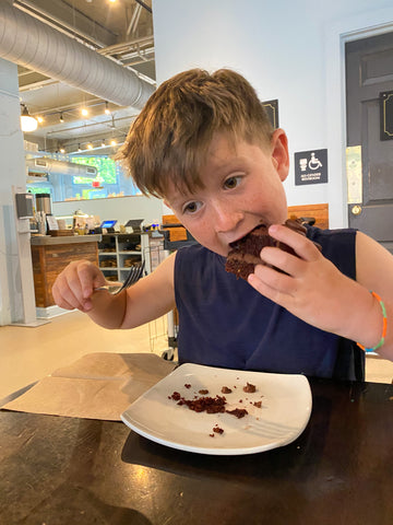 young boy stuffing face with chocolate peanut butter cake while holding a fork at French Broad Chocolate Lounge 