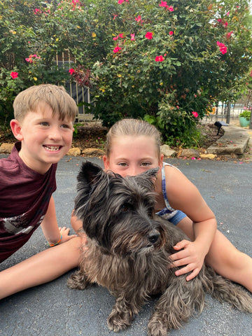 two young kids with black Cairn Terrier dog on driveway