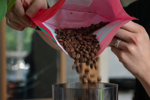 Vers gemalen koffiebonen - Iemand giet koffiebonen uit een roze zakje in een koffiemaler.