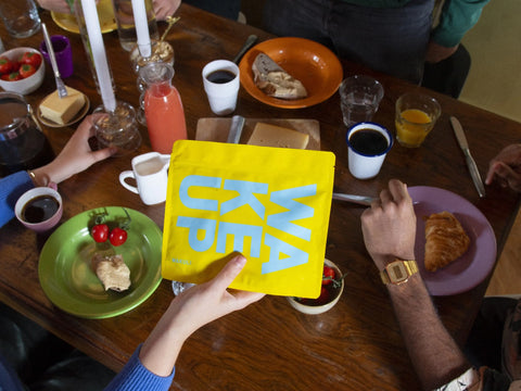 Koffie bewaren | Vrienden zitten rond een tafel te ontbijten. Eén van hen houdt een geel Wakuli zakje vast.