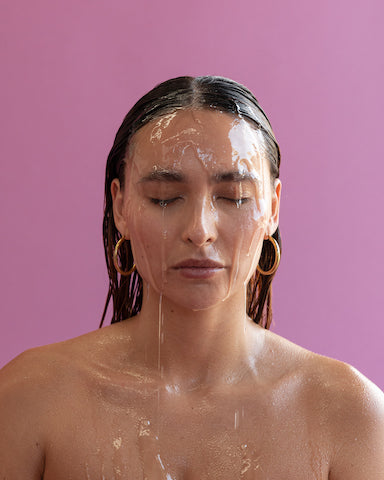 portrait of woman without clothes standing with her eyes closed while face serum is dripping 