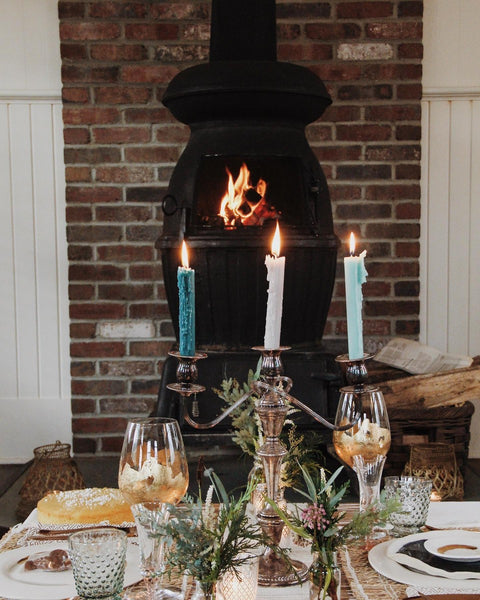 A winter table with blue candles and a lit fireplace.