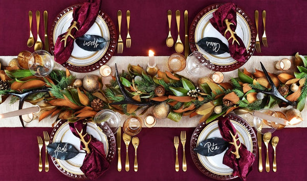 A moody and romantic tablescape featuring deep red colors, and a rustic garland lining the table.