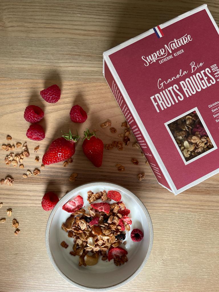 Bowl of granola with berries beside its packaging on a wooden surface.