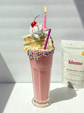 Birthday Cake Milkshake topped with a piece of birthday cake and candle on top, with a bag of Blume Birthday Cake Blend on the side.