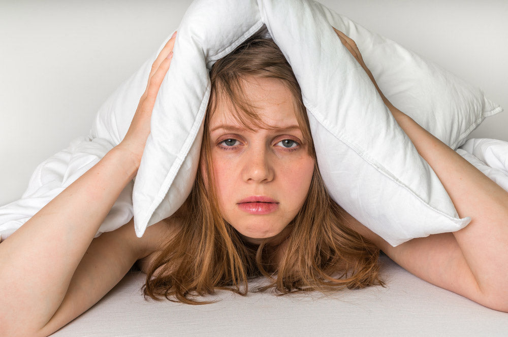 Frau mit Kissen über dem Kopf - Schlafprobleme