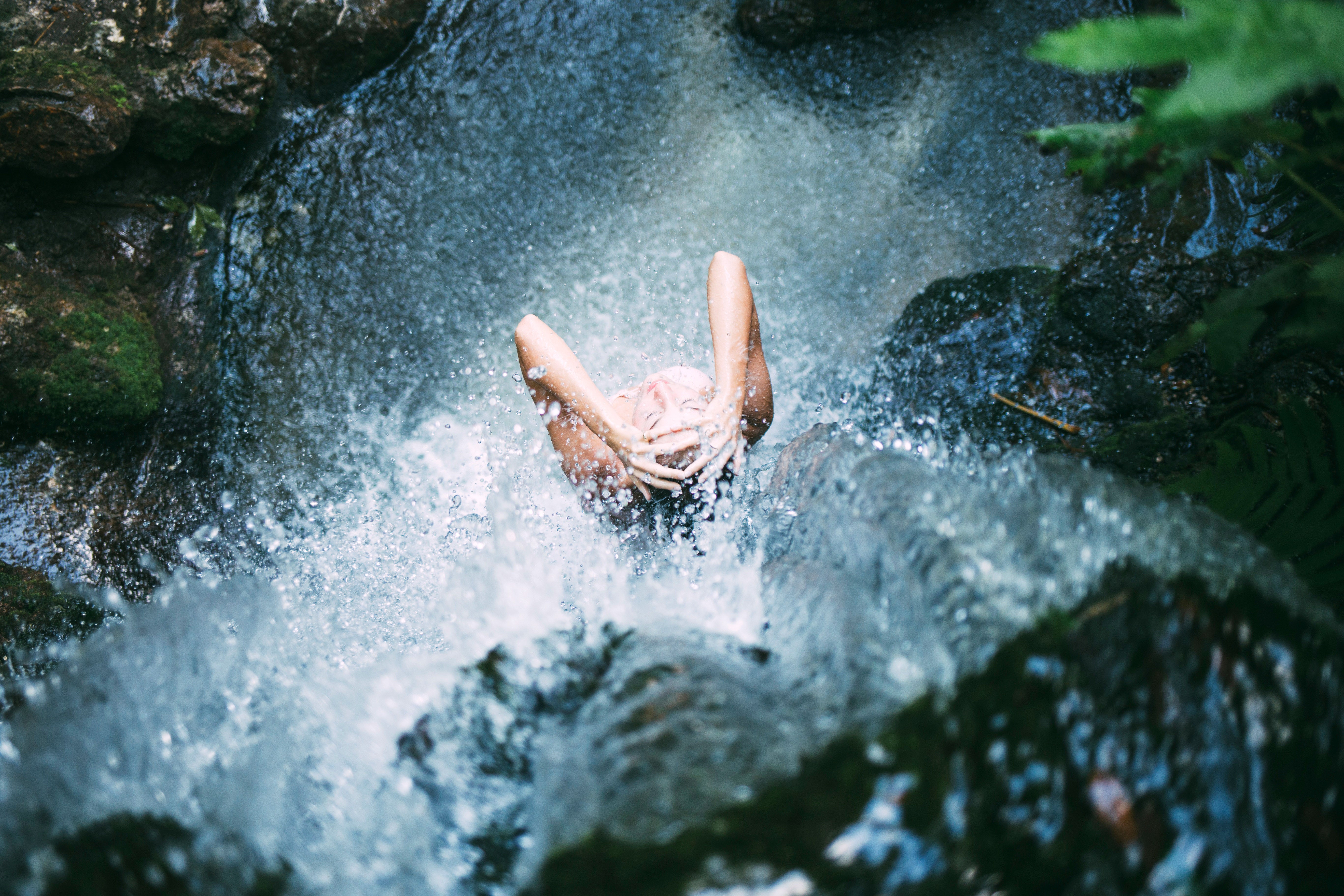 Frau duscht unter dem Wasserfall als leichte Abkühlung