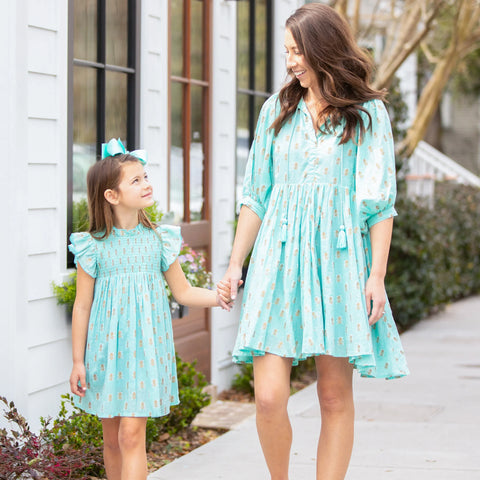 mom and daughter walking hand in hand in teal dresses down a sidewalk