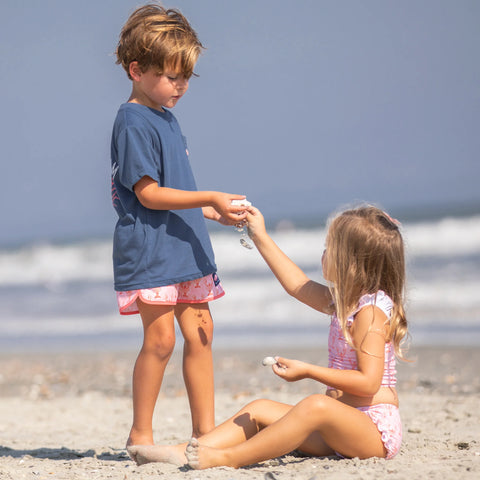 little boy standing up and a little girl sitting down on the beach