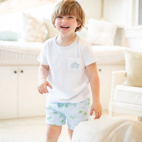 little boy laughing wearing a white tshirt with a turtle on it and lighth blue shorts with turtles
