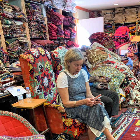 Hilly sat working in the middle of an Indian fabric store. Bright and beautiful fabrics piled high around the room