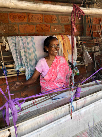 Indian lady wearing a pink sari standing behind a weaving loom