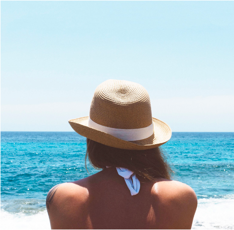 Woman on the beach in a straw hat looking out at the ocean. 