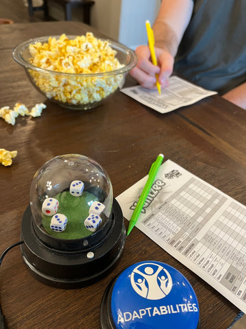 Switch adapted dice roller sits on a table along with two Yahtzee score cards, pencils, and a bowl of popcorn.