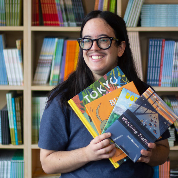 A photo of Basil holding up copies of some of their favourite books, including Tokyo Digs a Garden and Fern and Horn.