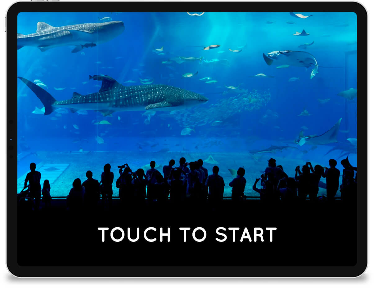 An iPad displaying a 'touch to start' message in front of a photo of an aquarium tank.