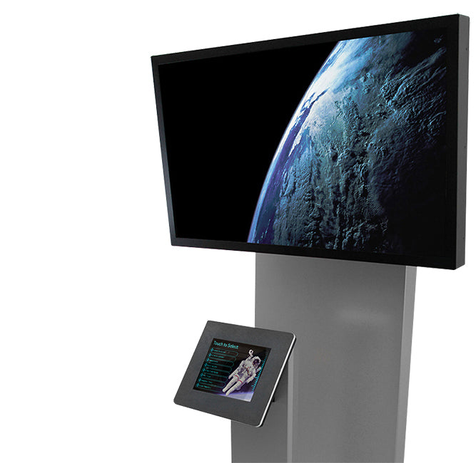 A standing kiosk enclosing both an iPad and a separate monitor. The iPad displays a selection menu while a video plays on the separate display.