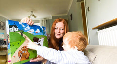 A mother and son read the gingerbread man kamishibai story. The mum holds the pages and the little boy is pointing to the hare.