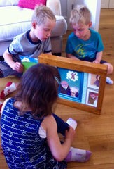 Two boys are reading the gingerbread man kamishibai, which is in a wooden frame on the floor, to a younger girl 