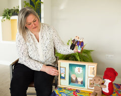 Wendy is holding the little old man and the little old woman props. She is about to turn the page of the kamishibai which is in a wooden frame sitting on a table with a crochet fox