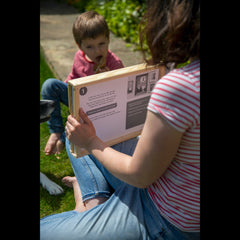 A mum holds the gingerbread man kamishibai story in a frame and is reading to her son who is facing her eating a gingerbread man biscuit