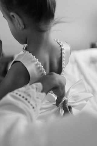 Close up look at how a woman is attaching a big bow at back of the flower girl dress decorated with artificial pearls