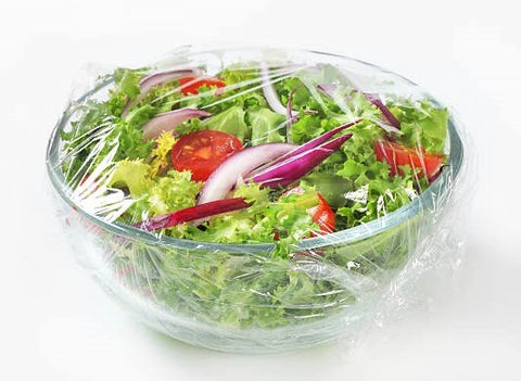 plastic wrap being used on a container with salad