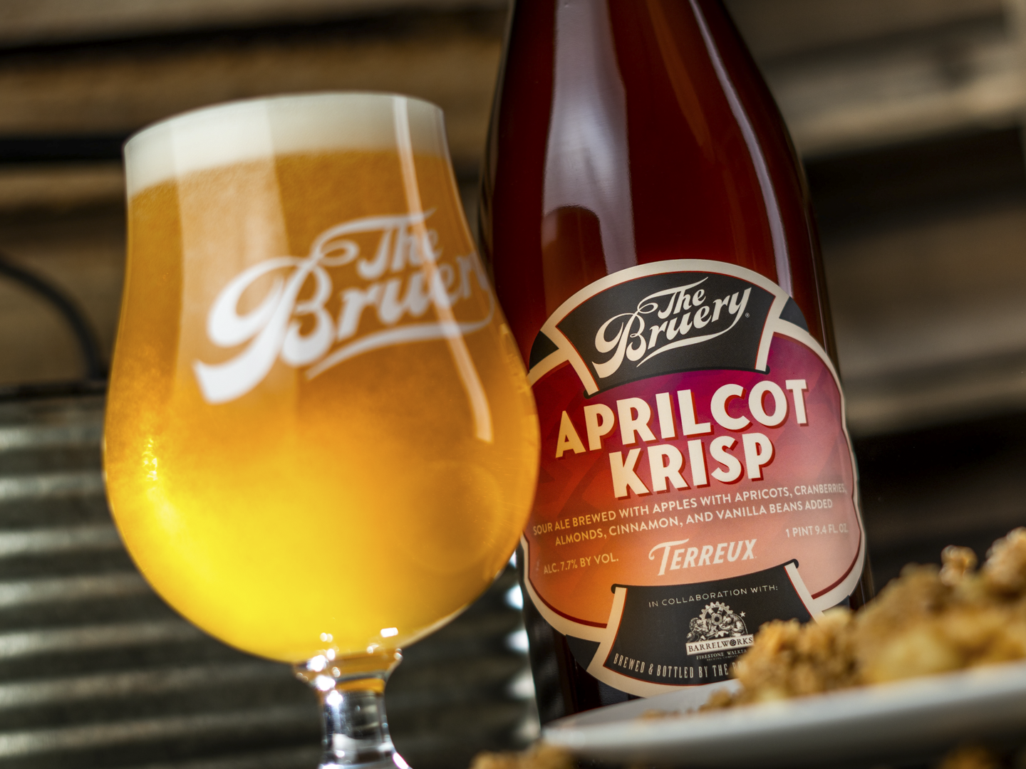 Closeup of pink and black Aprilcot Krisp label on the bottle with a glass of bright beer next to it.