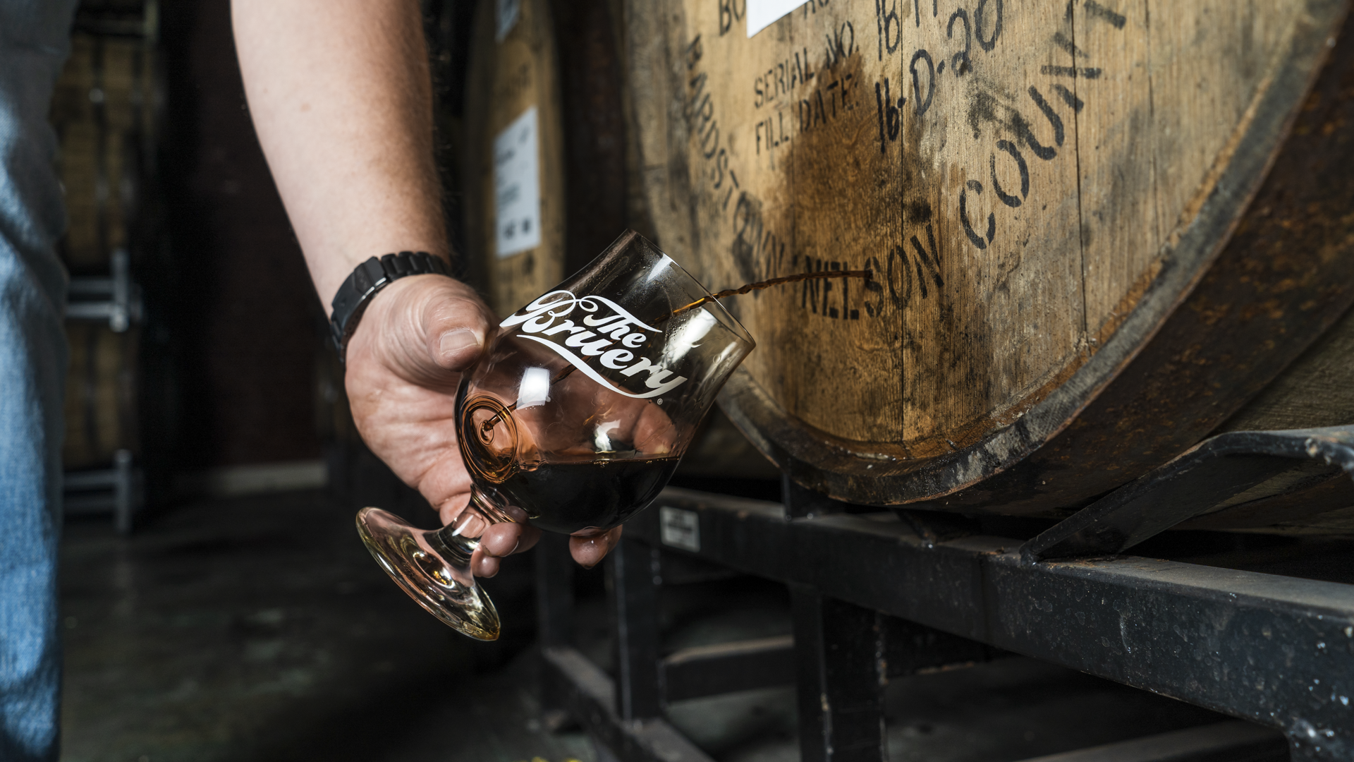 Photo of liquid pouring from a nail hole in a barrel into a Bruery branded glass.