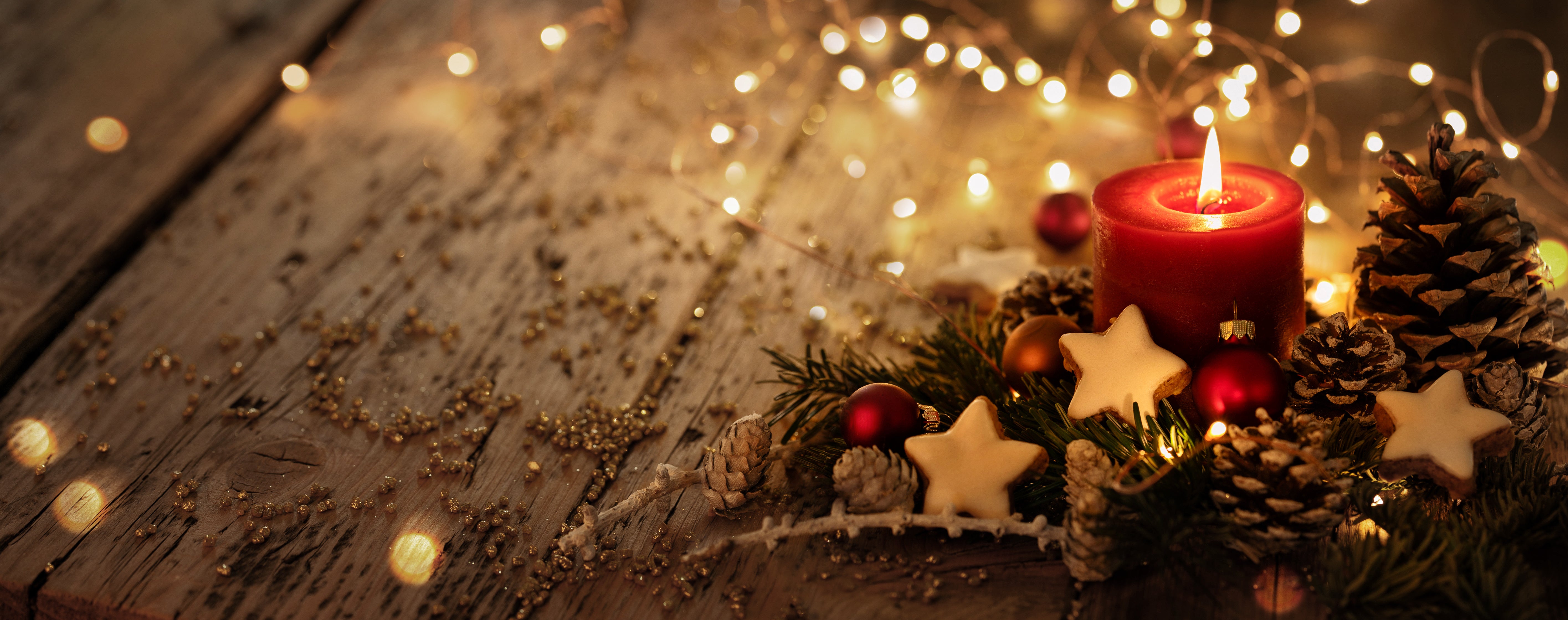 Weihnachtskerze mit Tannenzapfen und Lichtern auf einem Holztisch.