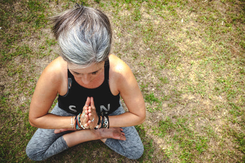 Frau mit grauen Haaren und Sportsachen sitzt in Yogapose auf einer Wiese