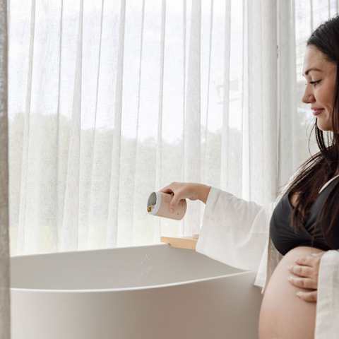 A pregnant woman pours pregnancy bath salts into a bathtub. 