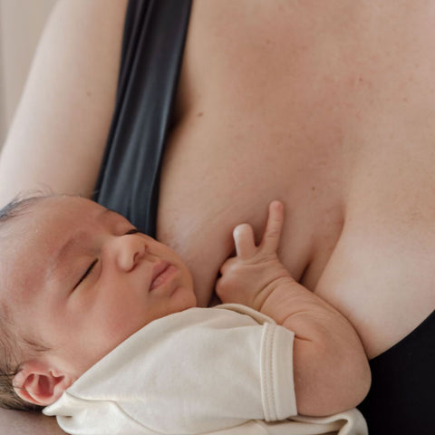 A newborn baby is cradled against its mothers chest. It holds a hand on her breast and could have just been breastfeeding.