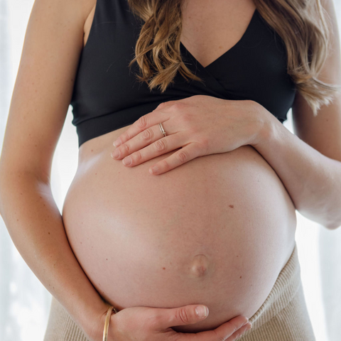 A focus on a pregnant mum-to-be holding her baby bump. She is wearing maternity underwear and could be preparing for birth and sorting out her birth plan.