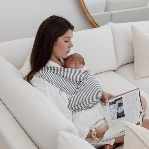 mother with her new baby in a chekoh baby wrap carrier sitting reading a book hands free