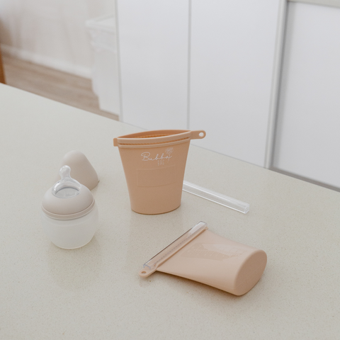 Reusable breast milk pouches and baby bottles sit on a bench. They are essential items for baby and could be added to an online baby gift registry.