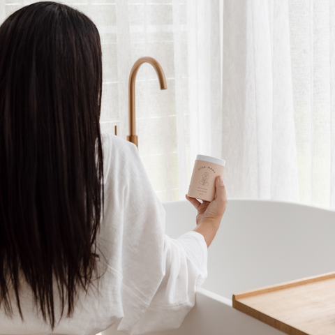 The back of a new mum standing over a bathtub. She is preparing for having a bath after birth, and holding a herbal mix for a sitz bath for recovery after labour and birth. 