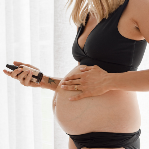 soon to birth pregnant woman rubbing belly oil on her growing belly.