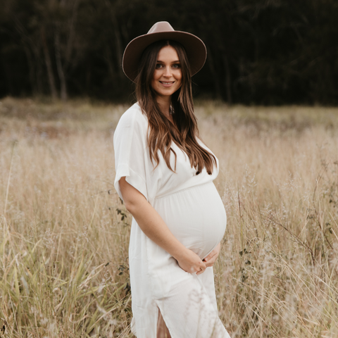 pregnant alana co founder of mother's mylk and author of nourished postpartum naturopath pregnant with her second son and holding her belly in a field.