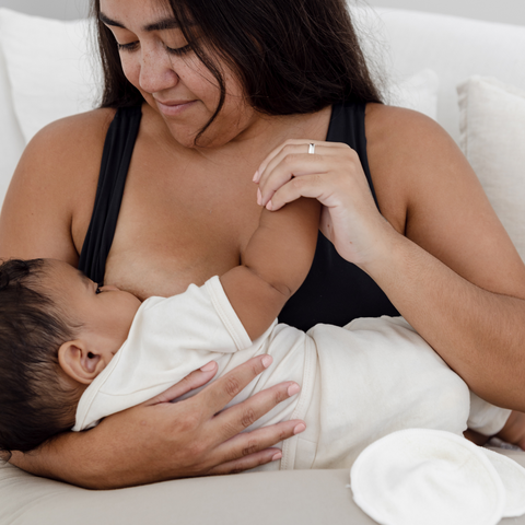 A mum and baby bond during breastfeeding. The baby is propped up on a breastfeeding support pillow. 