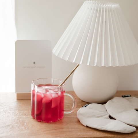 A red glass of nursing tea on a bedside table. Breast inserts for mum are also on the table, as a breastfeeding affirmation cards. 