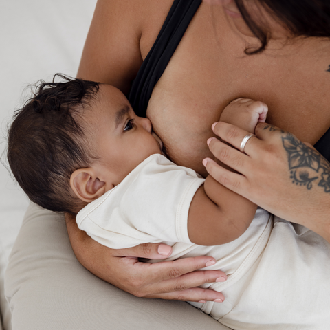 Baby breastfeeding and latching on the mother’s breast during feeding. The baby is held up by a breastfeeding support pillow with breastfeeding pads nearby. 